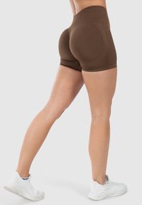 Bruine high-waisted shorts met een naadloos ontwerp, geschikt voor sportkleding. Gladde textuur en aansluitende pasvorm. Witte sportschoenen.
