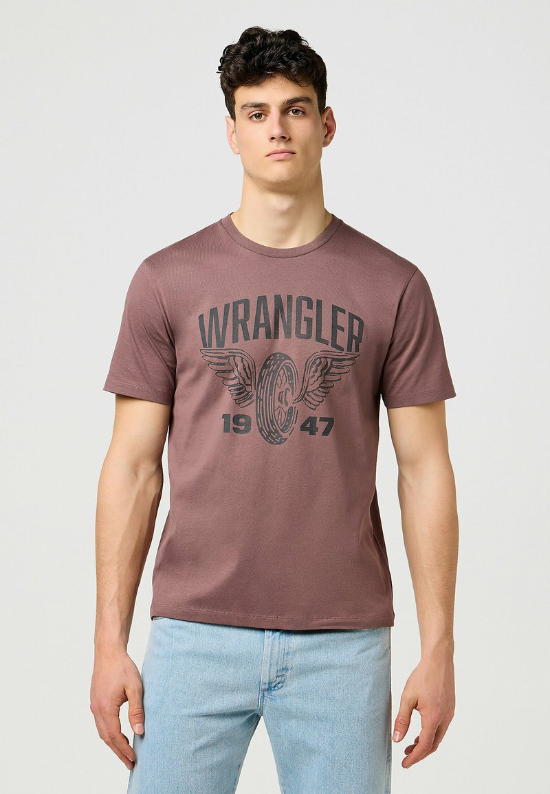 Brun kortärmad t-shirt gjord av mjukt tyg med en stor svart "WRANGLER" logotyp och vingdesign med "1947" under.