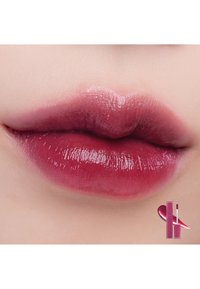 Des lèvres bourgogne brillantes avec un léger dégradé, une texture lisse et une forme pleine, avec un produit pour les lèvres affiché dans le coin.