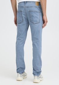 Svetlo modre kavbojke iz jeansa imajo kroj s pravimi hlačnicami, pet žepov in usnjen označevalni trak na zadnji strani pasu. Tkanina je gladke teksture.