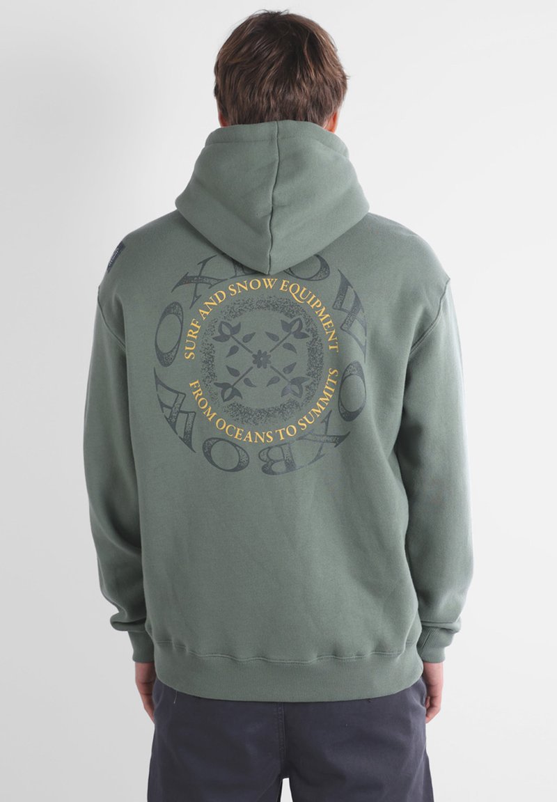 Hoodie vert olive avec un grand motif au dos, affichant "Équipement de Surf et de Neige" en texte circulaire jaune et gris foncé. Texture douce.