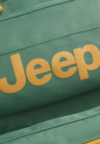 Tela verde con una superficie texturizada que presenta la palabra "Jeep" en letras amarillas y en negrita en el centro.