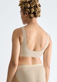 Beige sömlös bralette med breda band, djup rygg och mjuk textur. Matchas med höga trosor.