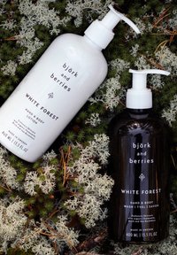 Zwei Flaschen auf Moos: eine weiße Pumpflasche mit "White Forest" Hand- und Körperlotion und eine schwarze Pumpflasche mit "White Forest" Hand- und Körperwaschmittel.