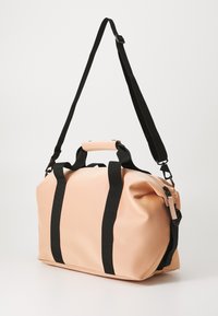 Ferskenfarget vanntett bag med svarte webbed stropper og et håndtak på toppen. Designet er mykt, med en rund form og en sømløs finish.
