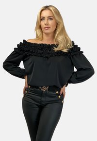 Czarna bluzka bez ramiączek z warstwowym detalem falbany, zestawiona z dopasowanymi czarnymi spodniami z złotymi guzikami na talii.