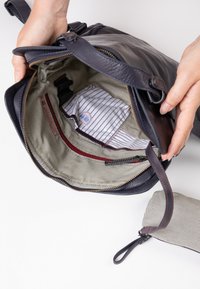 Marine leren tas met een grijs gestreepte binnenkant, voorzien van een rits, zakken en een kleine bijpassende tas aan de zijkant.