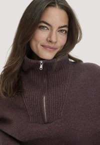 Paarse gebreide sweater met een hoge kraag, voorzien van een rits tot halverwege, ribbelstructuur en een soepel middenstuk.
