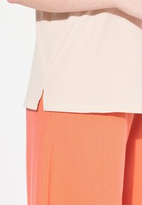 Camiseta de algodón beige con aberturas laterales, combinada con pantalones sueltos de color naranja brillante, confeccionados en una tela texturizada.