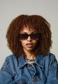 Svarta överdimensionerade solglasögon med gradientlinser, tjocka plastbågar. Bärs med en jeanjacka och ett silverkedjehalsband, mot en neutral bakgrund.