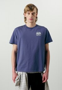 Camiseta de algodón azul marino con cuello redondo y mangas cortas. Presenta un pequeño logo impreso en blanco en la parte izquierda del pecho.
