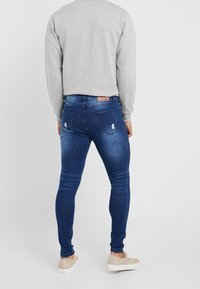 Vaqueros skinny azul oscuro con ligero desgaste en los bolsillos traseros, combinados con una sudadera gris y zapatos beige.