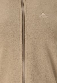 Beige fleecejakke med en frontlynlås og en diskret broderet bjerglogo på øverste venstre bryst.