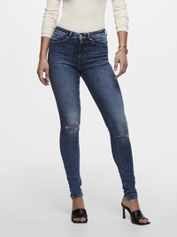 Mørkeblå skinny jeans med høy midje, med slitte knær, fem lommer og sølvfarget detaljer, parret med svarte åpne hæler.