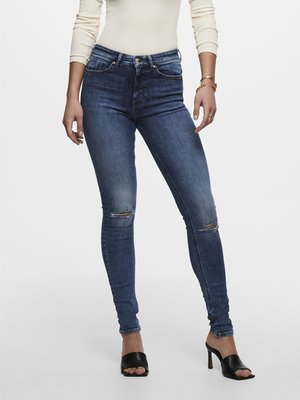 Mørkeblå skinny jeans med høy midje, med slitte knær, fem lommer og sølvfarget detaljer, parret med svarte åpne hæler.