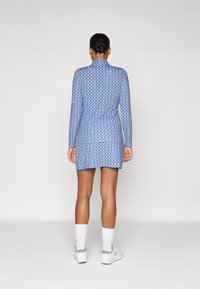 Long-sleeve blue dress with a textured, patterned design. Features a high collar and a layered skirt, paired with white socks and shoes.