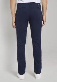 Tmavě modré slim-fit kalhoty z lehkého materiálu, s kapsami na zadní straně a čistým designem pasu, spárované s bílými teniskami.