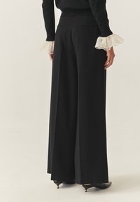 Zwarte brede broek met een tailored ontwerp, voorzien van een hoge taille en zijzakken, gecombineerd met sheer gerimpelde mouwen op een zwart top.