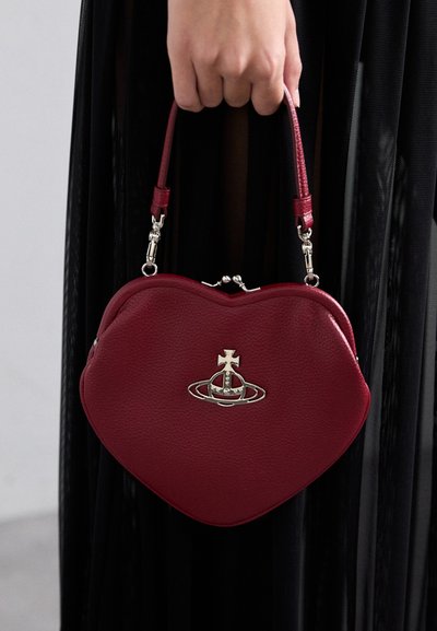 Sac en cuir rouge texturé en forme de cœur avec un logo décoratif en argent, une courte poignée et une fermeture à fermoir. Légère brillance et finition lisse.