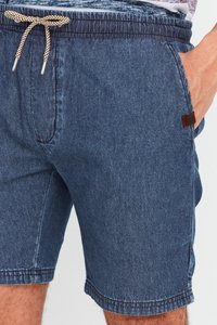 Pantaloni șort din denim cu o nuanță albastru închis, având o talie elastică cu un șnur contrastant și buzunare laterale. Include o etichetă de brand subtilă.