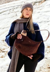 Brown leather bag with a textured, crocodile pattern and a short strap; held by a person wearing a blue sweater and gray scarf.