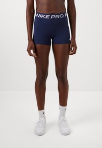 Marinefarvede Nike Pro shorts med en bred grå talje. Glat, strækbart stof, tætsiddende design og et lille logo på nederste venstre ben.