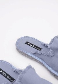 Sandales à glissière en tissu bleu clair avec des bords effilochés, des détails tissés et une semelle intérieure en textile. Présente une étiquette de logo noire sur le côté intérieur.