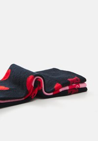 Chaussettes navy avec des motifs de points rouges et roses, présentant une texture douce et un design replié affichant des bords en tissu rose exposés.