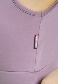 Top ajustado de color púrpura claro con cuello redondo y tejido texturizado. Una pequeña etiqueta que dice "SMILOOX" está cosida en la costura lateral izquierda.