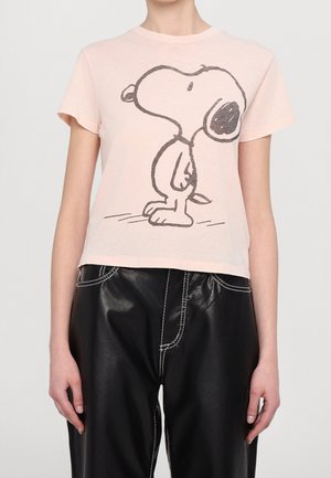 Osoba ubrana w jasnoróżowy t-shirt z czarno-białą kreskówką Snoopy'ego oraz czarne spodnie z białymi przeszyciami.