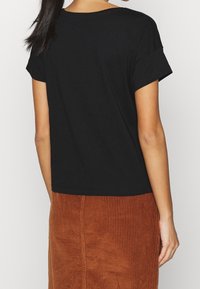 Černé tričko s krátkými ohrnutými rukávy, s volným střihem. V kombinaci s texturovanou sukní z kordu v barvě rezavé.