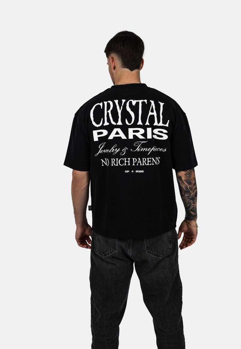 Černé oversized tričko s bílým textem na zadní straně: "CRYSTAL PARIS Šperky & Hodinky BEZ BOHATÝCH RODIČŮ". Krátké rukávy, volný střih.