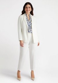 Witte blazer en broek gecombineerd met een blauw-wit gestreepte blouse. Het ensemble heeft zorgvuldig afgestemde lijnen en zachte texturen.