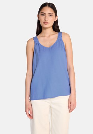 Blue, sleeveless top with V-neck and gathered detail at shoulder straps. Smooth fabric with relaxed fit, paired with cream-colored bottoms.