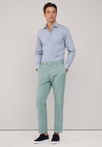 Lichtblauw en wit gestreepte overhemd met kraag, gecombineerd met mintgroene broek en donkere sneakers, met een getailleerd ontwerp en knoopaccent.