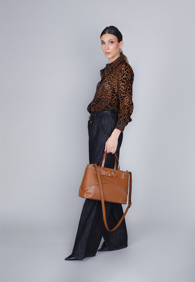Borsa a tracolla in pelle marrone con cuciture diagonali e tracolla staccabile, abbinata a una blusa con stampa leopardata e pantaloni larghi scuri.
