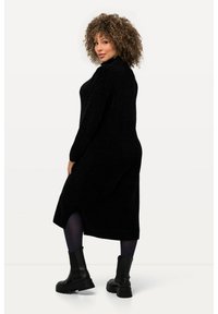 Lungo abito lavorato a maglia nero con collo alto e spacco laterale, in contrasto con collant neri opachi e stivali neri robusti. Tessuto con texture.