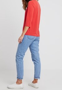 Rode driekwart mouwen t-shirt, gecombineerd met lichtblauwe rechte jeans en witte sneakers; casual fit en zachte stof.