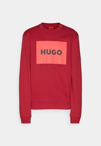 Sweat-shirt rouge à manches longues avec col rond, orné d'un grand rectangle corail et du texte noir audacieux « HUGO » centré sur le devant.