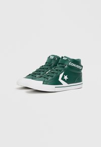 Zelené vysoké tenisky vyrobené z umělé kůže. Obsahují bílé akcenty, tkaničky a suchý zip označený "CONVERSE." Texturované boční panely.