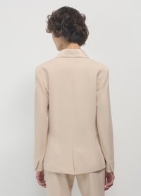 Beige Blazer mit tailliertem Design, Reverskragen und langen Ärmeln. Glatter Stoff mit einem Schlitz hinten.
