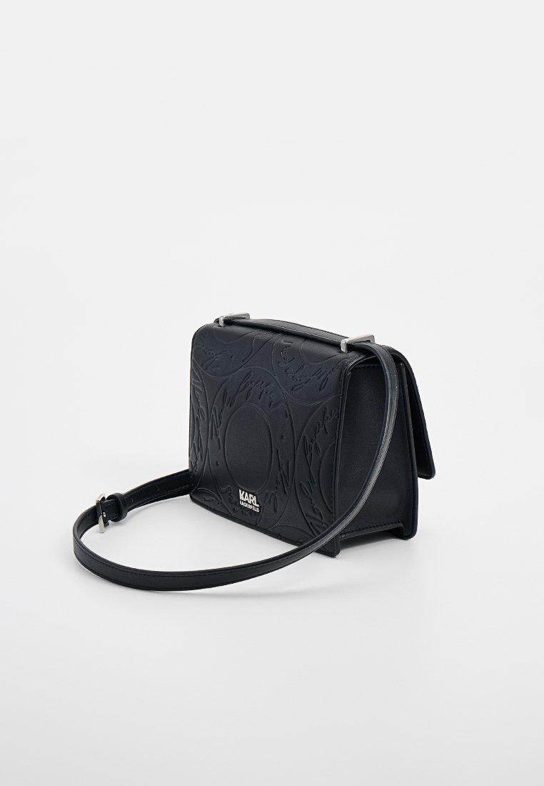 Borsa a tracolla nera di Karl Lagerfeld con motivo circolare embossato e tracolla regolabile su sfondo bianco uniforme.