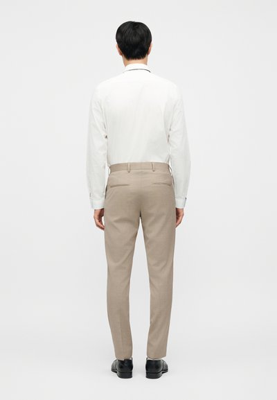 Μπεζ παντελόνια ραμμένα από απαλό ύφασμα, με κλασική εφαρμογή και δύο πίσω τσέπες, συνδυασμένα με λευκό πουκάμισο μακρυμάνικο.