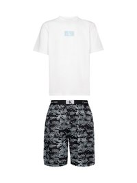 Maglietta bianca in cotone con logo CK azzurro chiaro sul petto, abbinata a pantaloni corti neri con un motivo astratto in azzurro chiaro e bianco.