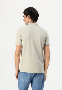 Lys grå polo skjorte med korte ermer og krage, laget av glatt stoff. Skjorten har sidespalter og en avslappet passform. Brukt med blå jeans.