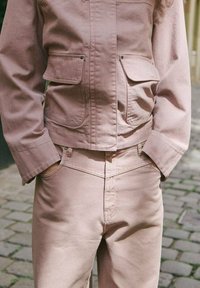 Różowa dżinsowa kurtka z dwoma przednimi kieszeniami i zapięciem na guziki, zestawiona z dopasowanymi różowymi dżinsami. Luźny krój i gładka tekstura.