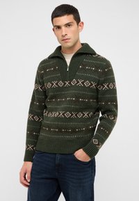 Zelený pletený sveter so zipsom na golieri, zdobený geometrickým vzorom v hnedej a krémovej farbe. Rebrované manžety a lem zvyšujú textúru.