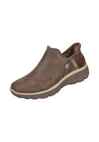 Zapato marrón tipo slip-on con una upper suave tipo gamuza, cuello acolchado y suela de goma con un patrón de relieve prominente para mayor agarre.
