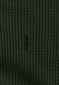 Dark green knitted fabric with a ribbed texture, featuring a small black embroidered letter 'F' on the front.