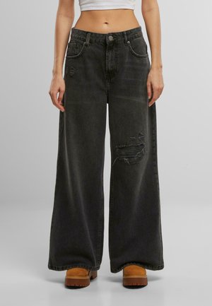 Wide-leg black denim jeans featuring a distressed detail on the front and a high waist, paired with tan platform footwear.